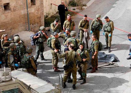 قوات الأمن الإسرائيلية تقف حول جثة فلسطيني في مسرح عملية طعن في مدينة الخليل بالضفة الغربية.