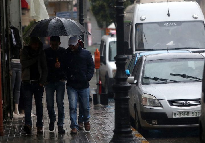 فلسطينيون يسيرون في شارع غمرته المياه في يوم ممطر في مدينة رام الله بالضفة الغربية