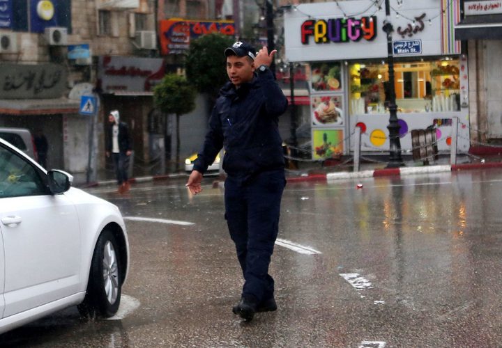 فلسطينيون يسيرون في شارع غمرته المياه في يوم ممطر في مدينة رام الله بالضفة الغربية