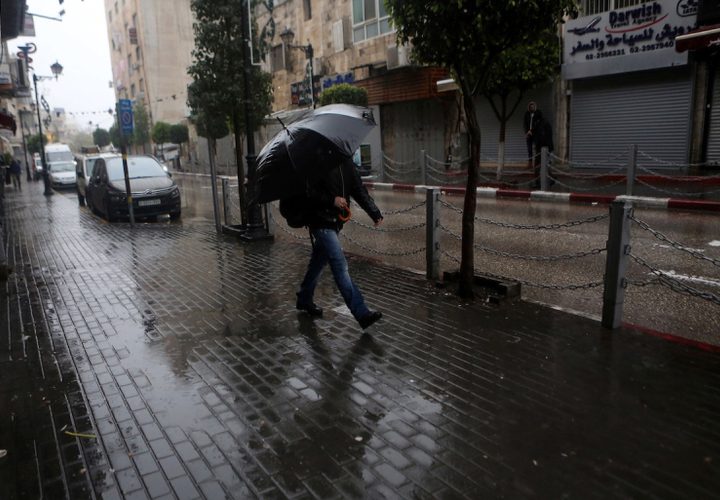 فلسطينيون يسيرون في شارع غمرته المياه في يوم ممطر في مدينة رام الله بالضفة الغربية