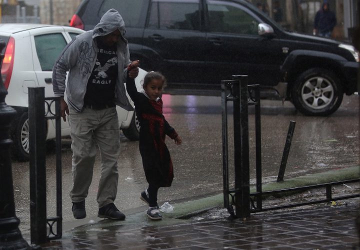 فلسطينيون يسيرون في شارع غمرته المياه في يوم ممطر في مدينة رام الله بالضفة الغربية