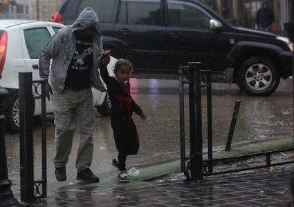 فلسطينيون يسيرون في شارع غمرته المياه في يوم ممطر في مدينة رام الله بالضفة الغربية