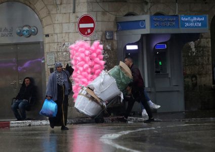 فلسطينيون يسيرون في شارع غمرته المياه في يوم ممطر في مدينة رام الله بالضفة الغربية