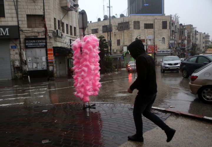 فلسطينيون يسيرون في شارع غمرته المياه في يوم ممطر في مدينة رام الله بالضفة الغربية