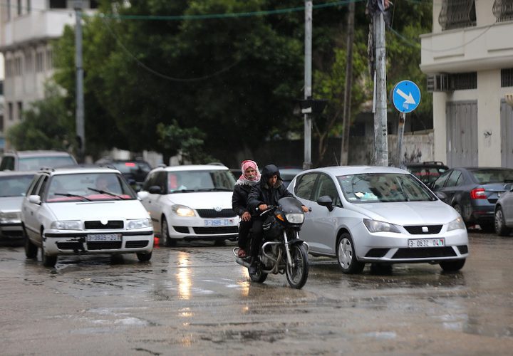 فلسطينيون يسيرون في شارع غمرته المياه في يوم ممطر في مدينة غزة