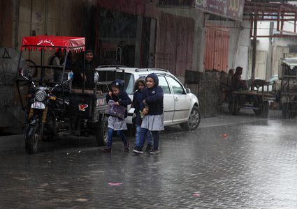 فلسطينيون يسيرون في شارع غمرته المياه في يوم ممطر في بيت لاهيا شمال قطاع غزة في 27 ديسمبر 2018.