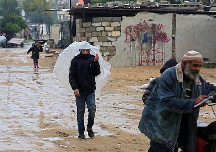 فلسطينيون يسيرون في الشارع في يوم ممطر في مخيم نهر البارد للاجئين في خان يونس جنوب قطاع غزة في 30 كانون الأول / ديسمبر 2018.
