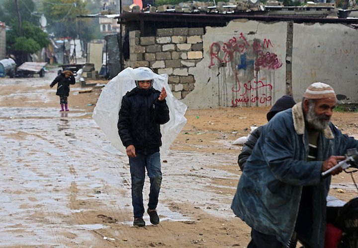 فلسطينيون يسيرون في الشارع في يوم ممطر في مخيم نهر البارد للاجئين في خان يونس جنوب قطاع غزة في 30 كانون الأول / ديسمبر 2018.