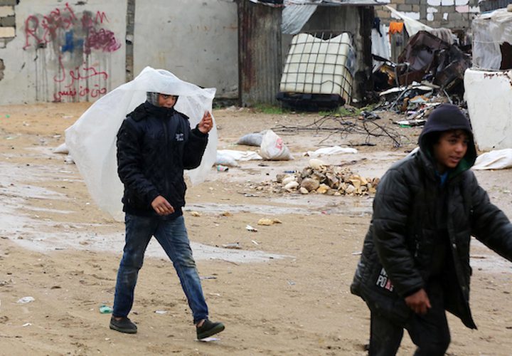 فلسطينيون يسيرون في الشارع في يوم ممطر في مخيم نهر البارد للاجئين في خان يونس جنوب قطاع غزة في 30 كانون الأول / ديسمبر 2018.