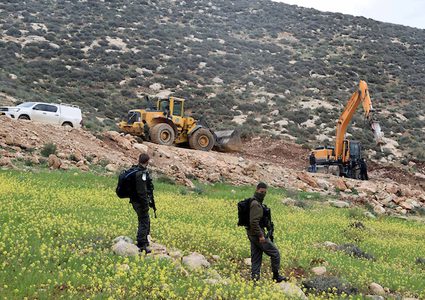 قوات الأمن الإسرائيلية تقف حارسة عندما تدمر جرافة تابعة للجيش الإسرائيلي تدمير الطريق في قرية يطا جنوب مدينة الخليل بالضفة الغربية في 11 فبراير / شباط 2019.