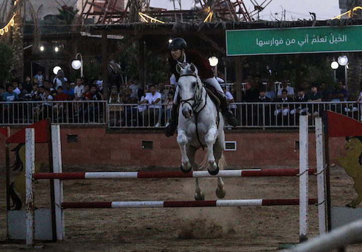 متسابقون فلسطينيون يقفزون مع أحصنتهم خلال مسابقة الفروسية المحلية ، في شمال مدينة غزة .