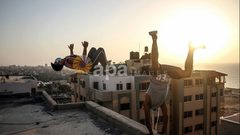 لاعبو باركور فلسطينيون يرتدون أقنعة ويظهرون مهاراتهم على سطح مبنى في مدينة غزة