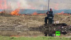 رجل يواصل صيد الأسماك رغم حريق يقترب منه