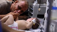 الفلسطيني محمد الحديدي يقبل يد طفله الناجي الوحيد من مجـزرة الشاطئ في غزة والتي راح ضحيتها 10 شهداء بينهم اطفال ونساء